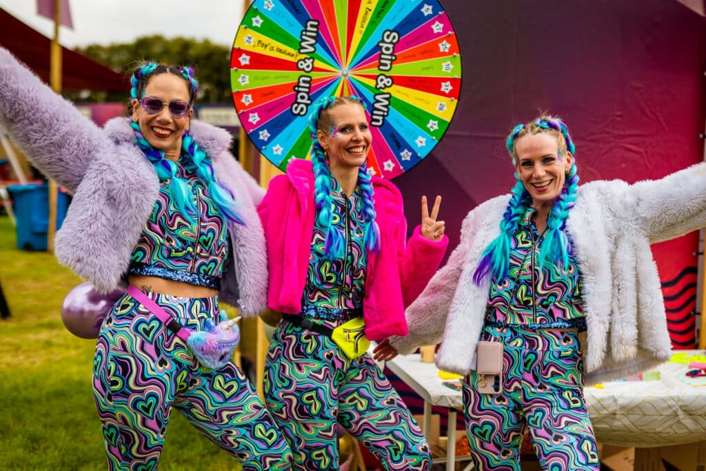 Drie bezoekers in glitteroutfits bij het rad van fortuin